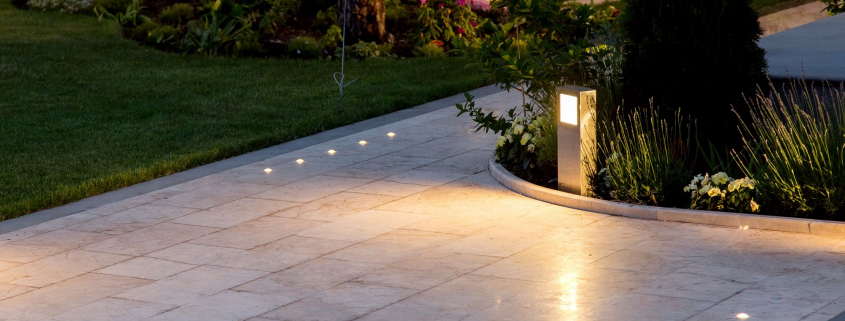 marble tile playground in the backyard of flowerbeds and lawn with ground lantern and lighting in the warm light at dusk in the evening.
